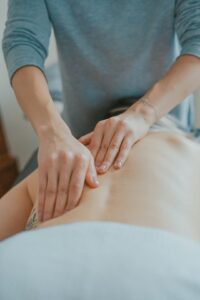 Students practice massage techniques on a training table while an instructor observes hand placement and body mechanics.