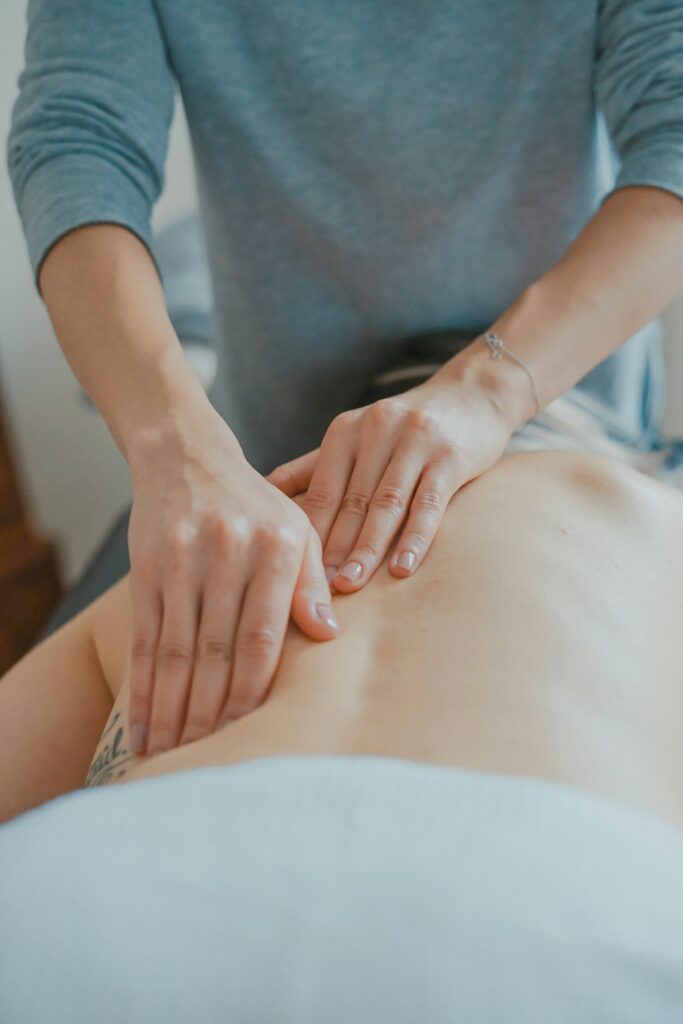 Students practice massage techniques on a training table while an instructor observes hand placement and body mechanics.